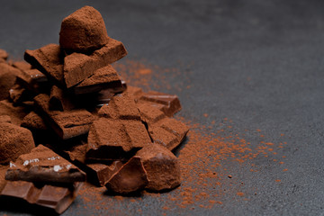 Dark or milk organic chocolate pieces, cocoa powder and truffle candies on dark concrete backgound