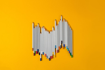 colored pencils arranged in a chaotic line on yellow background