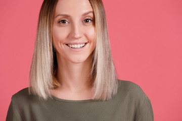 Cheerful pleasant looking girl has happy expression, dressed in green t-shirt, satisfied with good results after competition, talks with interlocutor, poses against pink studio wall