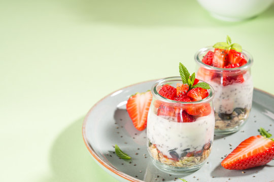 Yogurt granola parfait with strawberries and chia seeds. Healthy delicious dessert for breakfast. Mint green bright spring summer background
