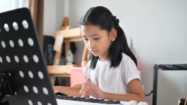 Asian little girl learning to play basic piano by using electric synthesizer keyboard for beginner music instrumental self studying at home