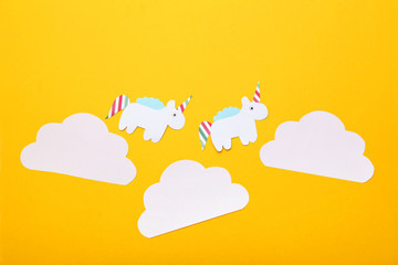 Paper unicorns and clouds on yellow background. Minimalism concept