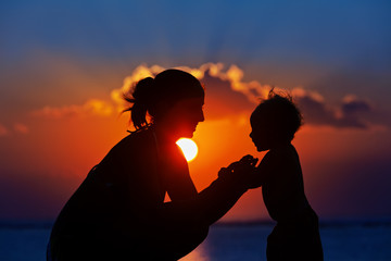 Happy family black silhouette on sunset sky background. Young mother, baby son have fun together,...