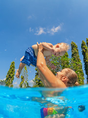 Happy family - mother trowing up in air and catch litle baby son. Training with fun in swimming...