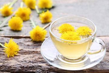 Yellow dandelions with cup of tea on wooden table