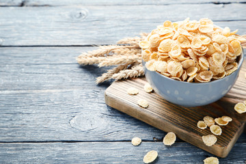 Corn flakes in bowl with wheat ears on grey wooden table
