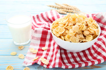 Corn flakes in bowl with glass of milk and wheat ears on wooden table