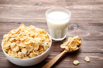 Corn flakes in bowl with glass of milk on brown wooden table