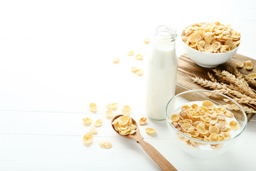 Corn flakes in milk with wheat ears on white wooden table