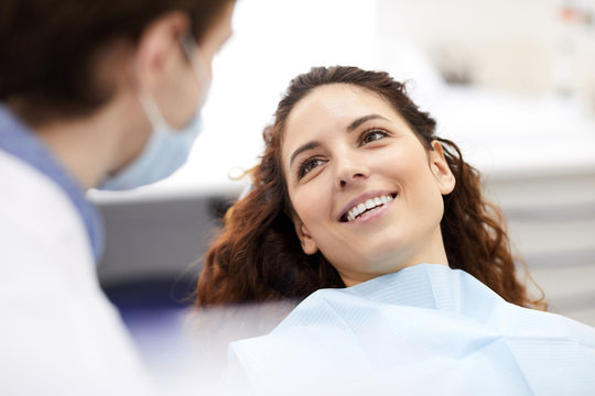 Head and shoulders portrait of smiling young woman lying in dental chair and looking at doctor, copy space
