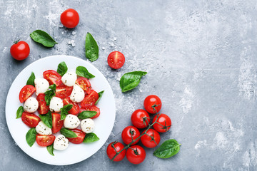 Mozzarella, tomatoes and basil leafs in plate on grey wooden table