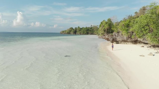 Aerial: woman walking on tropical island turquoise water white sand beach, Tomia Island, Wakatobi marine national park, Indonesia, Native cinelike D-log color profile