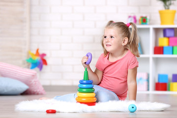 Little girl sitting on white carpet and playing with toys