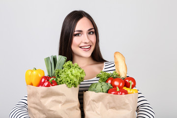 Beautiful woman holding grocery shopping bags on grey background
