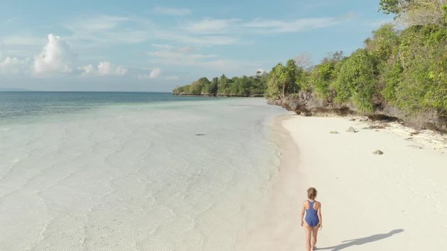 Aerial: woman walking on tropical island turquoise water white sand beach, Tomia Island, Wakatobi marine national park, Indonesia, Native cinelike D-log color profile
