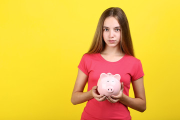 Fototapeta na wymiar Young girl holding pink piggybank on yellow background