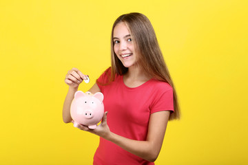 Young girl holding pink piggybank and coin on yellow background