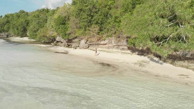 Aerial: woman walking on tropical island turquoise water white sand beach, Tomia Island, Wakatobi marine national park, Indonesia, Native cinelike D-log color profile