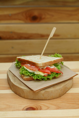 juicy sandwich with bacon, fresh vegetables, green salad and dark lines after grill on wooden plate