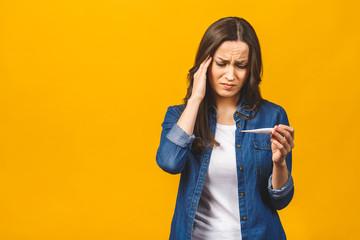 Young woman having flue taking thermometer. Isolated against yellow background. Beautiful young...