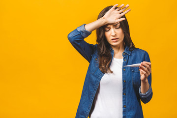 Young woman having flue taking thermometer. Isolated against yellow background. Beautiful young...