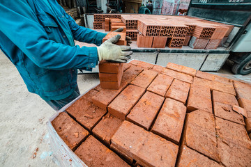 Construction worker unloading delivery truck lorry clay bricks at the building site warehouse