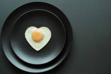 Delicious heart-shaped fried chicken egg on black ceramic plates on black background minimal style. Concept — cooking, gourmet, restaurant.