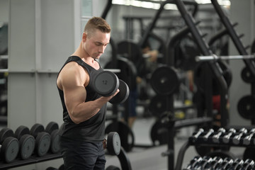 handsome man in good shape with muscles in the gym exercising exercises with dumbbells