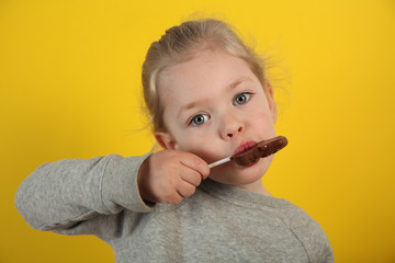 Cute girl child eating sweet chocolate candy on yellow background. Happy childhood.