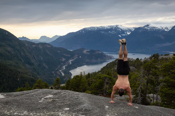 Fit and Muscular Young Man is doing exercises on top of the Mountain during a cloudy sunset. Taken on Chief Mountain in Squamish, North of Vancouver, BC, Canada.