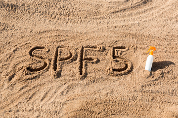Sun protect factor five. SPF 5 word written on the sand and white bottle with suntan cream. Skin care concept background