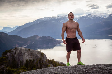 Fit and Muscular Young Man is on top of the Mountain during a cloudy day. Taken on Chief Mountain in Squamish, North of Vancouver, BC, Canada.