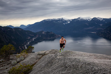 Fototapeta na wymiar Fit and Muscular Young Man is Running up the Mountain during a cloudy day. Taken on Chief Mountain in Squamish, North of Vancouver, BC, Canada.