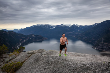 Fit and Muscular Young Man is Running up the Mountain during a cloudy day. Taken on Chief Mountain in Squamish, North of Vancouver, BC, Canada.