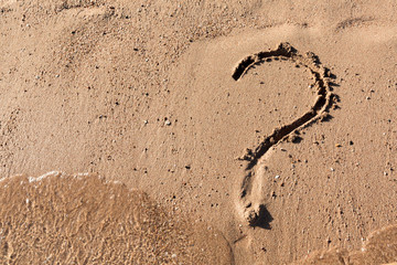 Question mark sign on sand beach near the sea. Concept of dilemma, answer and question