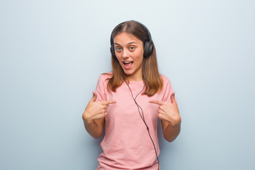 Young pretty caucasian woman surprised, feels successful and prosperous. She is listening to music with headphones.