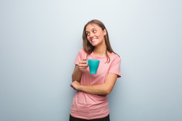Young pretty caucasian woman smiling confident and crossing arms, looking up. She is holding a mug.