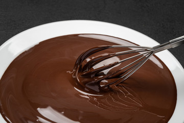 Macro of Melted milk or dark chocolate swirl in plate and whisk on concrete background