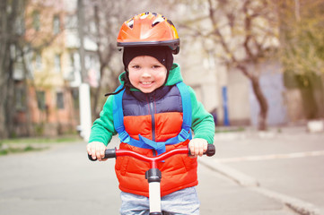 Fototapeta na wymiar Little cool boy in a helmet and a red vest riding a bicycle with a blue backpack on his back.
