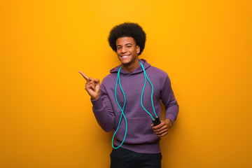 Young african american sport man holding a jump rope pointing to the side with finger