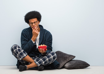 Young black man sitting and having a breakfast doubting and confused