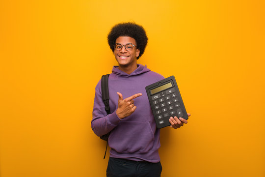 Young african american student man holding a calculator pointing to the side with finger