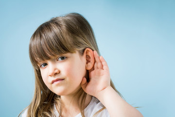 Fototapeta premium Toddler girl with hearing problem on light blue background. Close up, copy space.