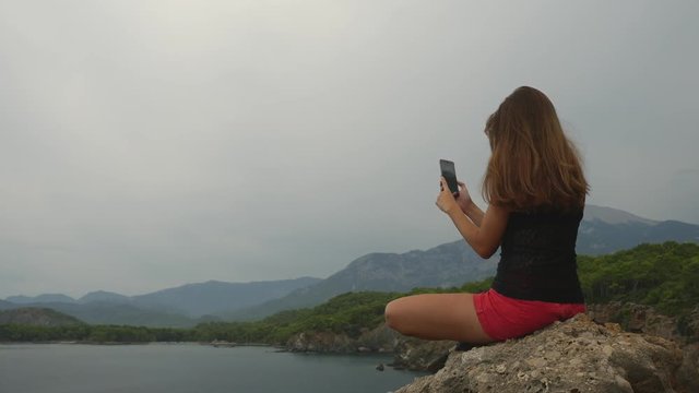 Female tourist sitting on a rock on clear sky and calm sea background