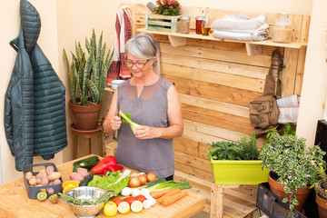 Happy senior woman gray hair clean and takes care of the vegetables harvested in the garden preparing a vegetable soup. Elderly retired people. Wooden table and background. Vintage style