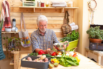 Old man, casual clothing, outdoors in the garden prepare a vegetable soup with a lot of potatoes,...