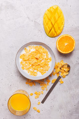 Breakfast which consist of different yellow ingredients - sereales and fruits. Gray background