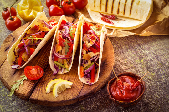 tacos  Mexican food with chicken, pepper, tomatoes, cabbage and salsa on a wooden Board
