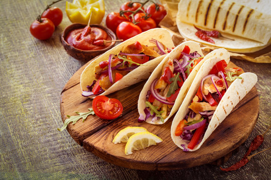 tacos  Mexican food with chicken, pepper, tomatoes, cabbage and salsa on a wooden Board