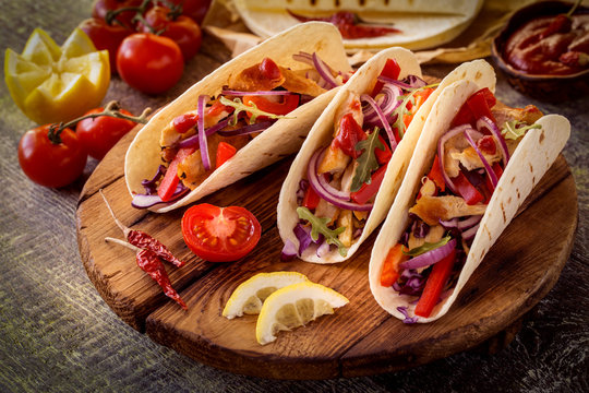 tacos  Mexican food with chicken, pepper, tomatoes, cabbage and salsa on a wooden Board
